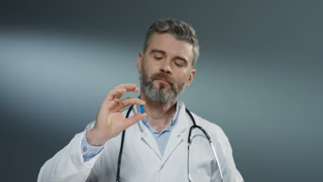 Caucasian-male-nice-cute-doctor-holding-two-pills-in-hands---yellow-and-blue---and-looking-at-them-like-comparing-and-choosing-blue-one.
